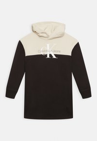 Mikina s kapucí s krémovou horní částí a černým dolním tělem. Obsahuje velké logo "CK" a bílý text "Calvin Klein Jeans".