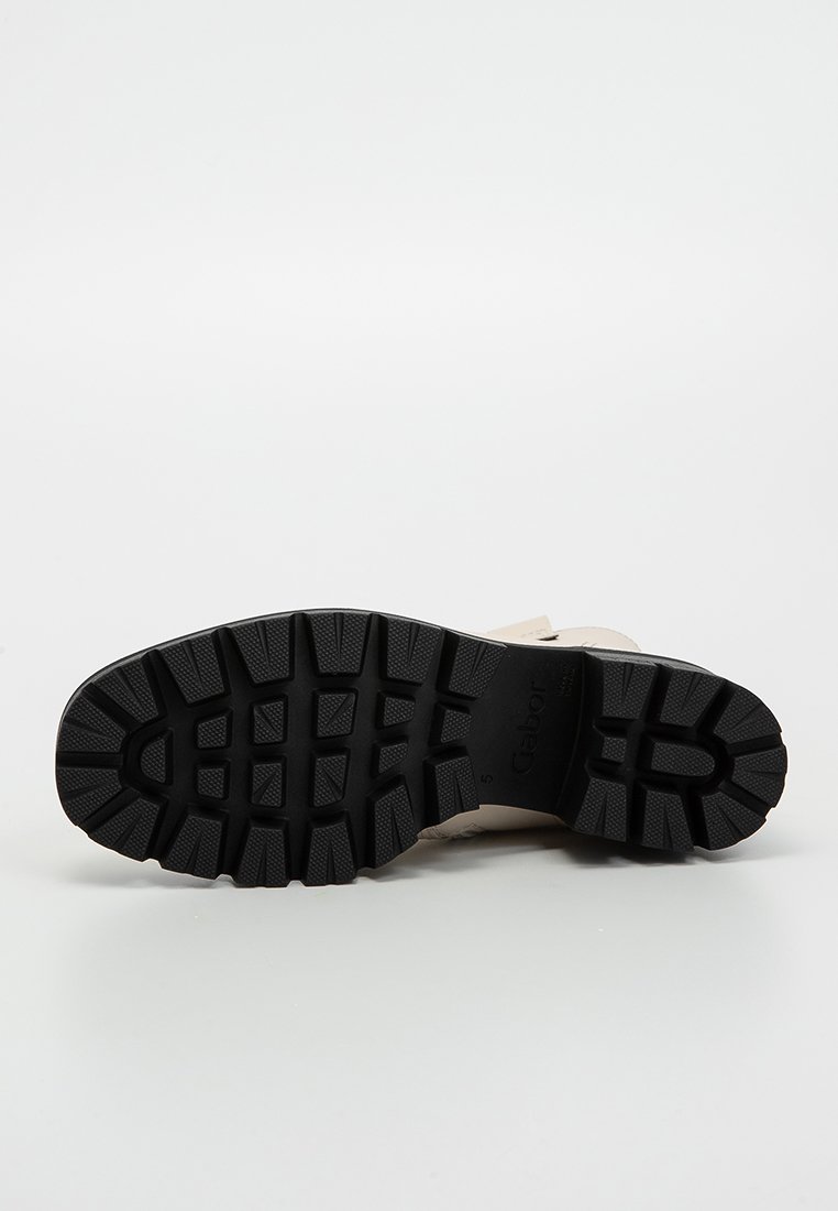 Schwarze Gummisohle mit tiefen Profilen, beigefarbene Obermaterial mit glatter Textur und minimalistischem Design. Markenlogo präge auf der Sohle.