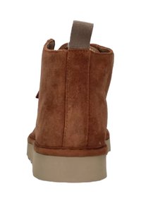 Stivaletto alla caviglia in suede marrone con suola in gomma beige. Presenta un cinturino ad anello sul retro e dettagli cuciti lungo i lati.