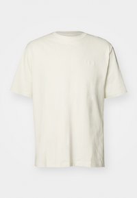 T-shirt couleur crème, à manches courtes et col rond, fabriqué en coton doux. Présente un logo discret brodé sur la poitrine.