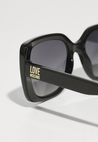 Fekete, oversized napszemüveg sötét lencsékkel. Fényes felülettel és arany színű "LOVE MOSCHINO" márkázással a szárán.
