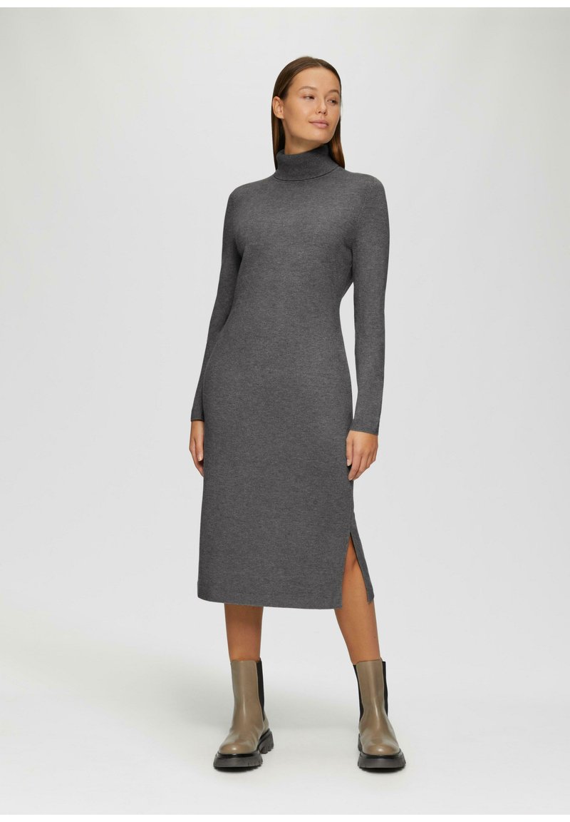 Grijze langemouwen jurk met een hoge hals, zijslitsen en een getailleerd silhouet, gemaakt van zacht materiaal. Gestyled met enkelhoogte zwarte en grijze laarzen.