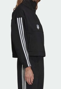 Svart sweatshirt med hög krage, vit tre-stripesdesign på ärmarna och en liten logotyp på bröstet. Har en avslappnad passform.