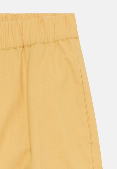 Gelbe elastische Bundhose mit glatter Textur und Seitentaschen, die ein einfaches Design und minimale Nähte aufweist.