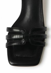 Sandalo in pelle nera con punta quadrata, caratterizzato da due cinghie testurizzate e una tomaia liscia. Design minimalista con tacco piatto.