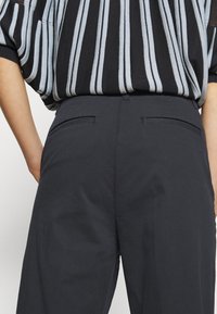 Tmavě šedé kalhoty s hladkým povrchem, vybavené bočními kapsami a přiléhavým pasem. Nosené s černým a světle modrým pruhovaným oversized topem.
