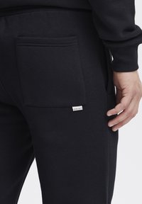 Black sweatpants made of soft fabric, featuring a side pocket and a small brand tag. The design is simple and functional.