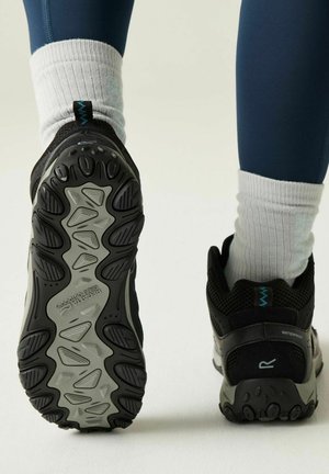 Stopy w czarno-szarych wodoodpornych butach trekkingowych z grubą podeszwą bieżnikową, w białych skarpetkach i granatowych legginsach.