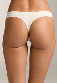 Tanga beige in tessuto liscio e elastico con un'ampia fascia in vita, che presenta un design minimalista e bordi senza cuciture.