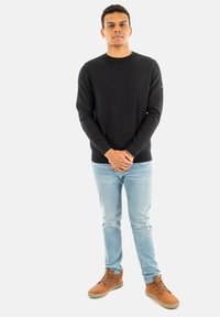 Maglione nero a maniche lunghe, design aderente, con collo a coste. Abbinato a jeans azzurri e stivali à la chelsea marroni. Look semplice e classico.