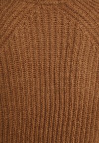 Gros plan d'un tissu tricoté marron doux et duveteux avec un motif côtelé vertical.