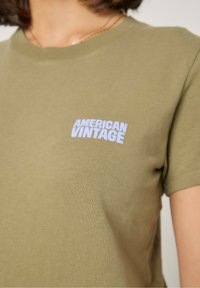 Olivovo zelené bavlnené tričko s krátkymi rukávmi, na hrudi s bielym logom "AMERICAN VINTAGE". Hladká textura, klasický strih.
