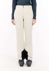 Beige skibroek met zwarte accenten, gemaakt van een zacht, flexibel materiaal. Voorzien van een knoopsluiting en een logo nabij de zoom. Soepele textuur.