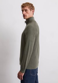 Olijfgroene ritssluiting sweater van textiel met een staande kraag en ribgebreide mouwen, gecombineerd met donkere spijkerbroeken.