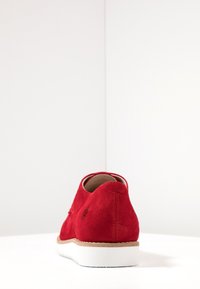 Červená semišová bota s kulatým siluetou a bílou gumovou podrážkou, vyznačující se hladkým povrchem a minimalistickým designem. Vhodná pro každodenní nošení.