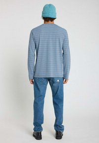 Chemise à manches longues rayée bleu et blanc, associée à un jean en denim bleu clair et des chaussures noires. Le modèle porte également un bonnet bleu clair.