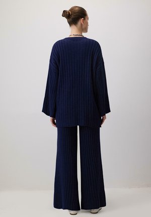 Tamnjenje rebraste pletene tunike sa širokim rukavima i odgovarajućim širokim hlačama. Tekstuirana tkanina, duža stražnja ivica i opušteni kroj.