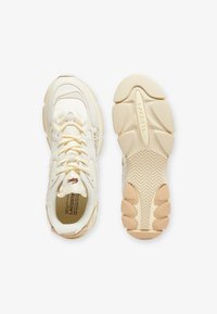 Crème-kleurige sneakers met een gestructureerde bovenkant, voorzien van een gewatteerde kraag, contrasterende branding en een chunky beige rubberen zool.