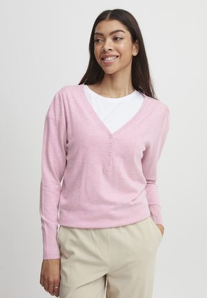 Ljust rosa v-ringad tröja i mjukt material, med knappslå och långa ärmar, tillsammans med krämfärgade byxor.
