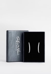 Silvriga snörörhängen presenterade i en svart sammetfodrad ask med ett texturerat grått lock, med varumärket präglat i vitt.