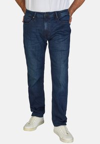 Jeans de mezclilla azul oscuro con un corte recto, que muestran un ligero desgaste y detalles de costura, combinados con zapatillas blancas.