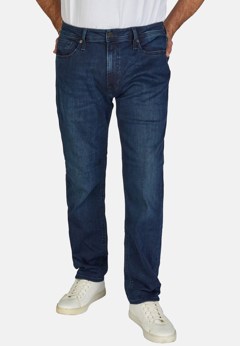 Jeans de mezclilla azul oscuro con un corte recto, que muestran un ligero desgaste y detalles de costura, combinados con zapatillas blancas.