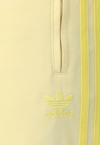 Pantalones deportivos amarillos con una textura suave, que cuentan con bolsillos laterales y rayas amarillas. El logo de Adidas está bordado en un tono a juego.