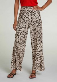 Leopardmønstret bukser i beige med sorte pletter, med en bred ben-design og letvægtsstof, parret med sorte sandaler med stropper.