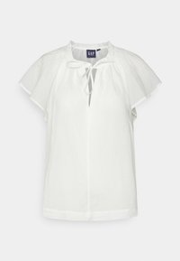 Blouse blanche à manches courtes avec coupe ample, col volanté, décolleté en forme de clé avec lien et étiquette GAP à l'intérieur du col.