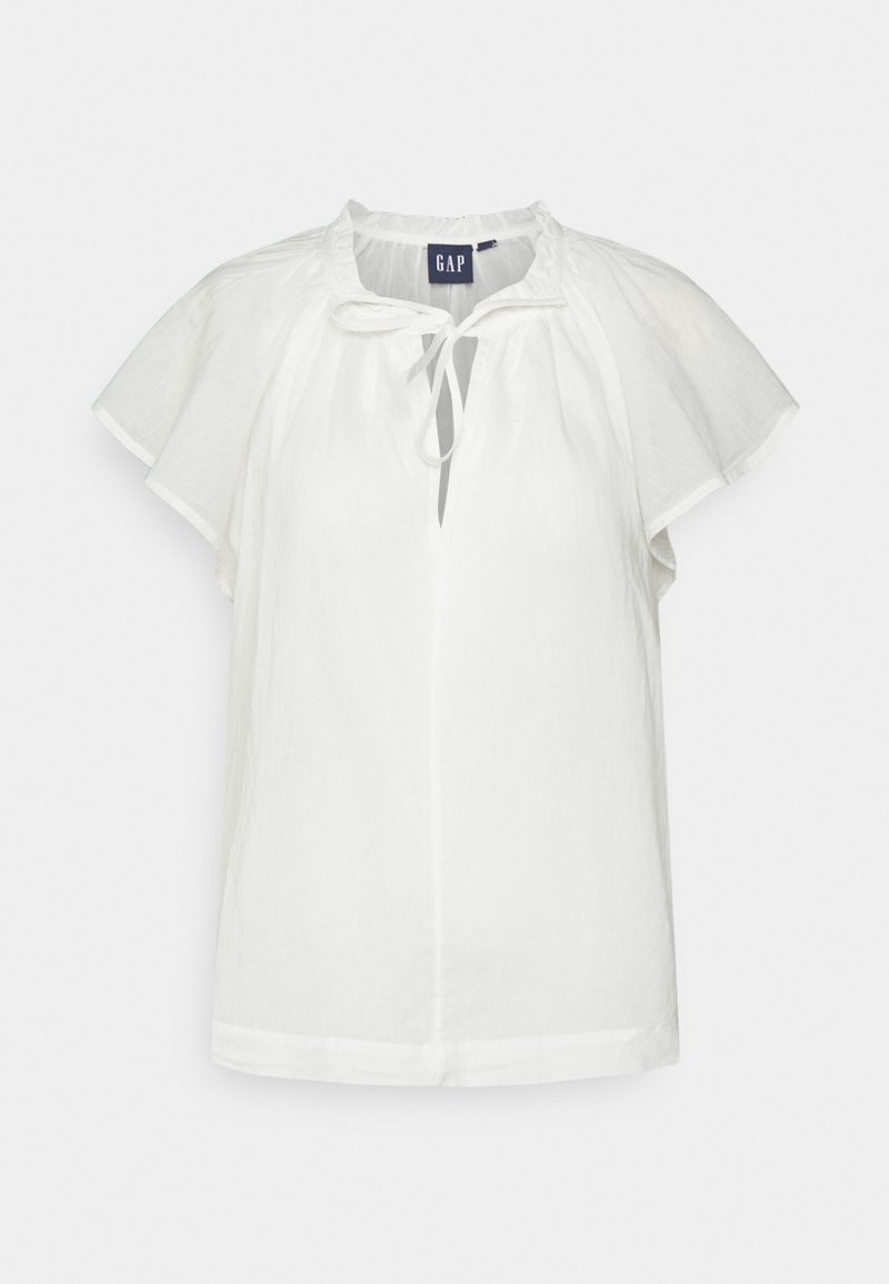 Blouse blanche à manches courtes avec coupe ample, col volanté, décolleté en forme de clé avec lien et étiquette GAP à l'intérieur du col.