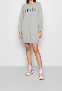 Robe sweat-shirt grise avec le logo "LEVI'S" en lettres colorées. Comprend des manches longues et un ourlet côtelé. Associée à des baskets montantes roses.