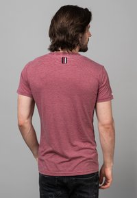 Maglietta a maniche corte a righe rosse con collo rotondo e una piccola toppa decorativa con tre righe verticali sulla schiena.