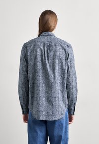 Langsleeve shirt in blauw met een wit patroontje. Beschikt over een kraag met knopen en een rechte zoom. Gemaakt van een lichtgewicht stof.