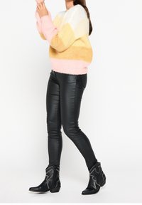 Färgglad stickad tröja med rosa, gult och vitt randigt mönster, ihop med svarta fake läder leggings och svarta anklarstövlar med dekorativ söm.