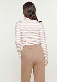 Maglietta a maniche lunghe a righe in un delicato rosa e bianco, abbinata a pantaloni elasticizzati beige chiaro con vita elastica, che mostrano una vestibilità comoda e una morbida texture.