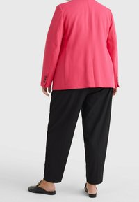 Różowa marynarka o usztywnionym kroju, z pojedynczym rozcięciem z tyłu i czarnymi, zwężającymi się spodniami. Obuwie to czarne, półbuty z odkrytymi piętami.