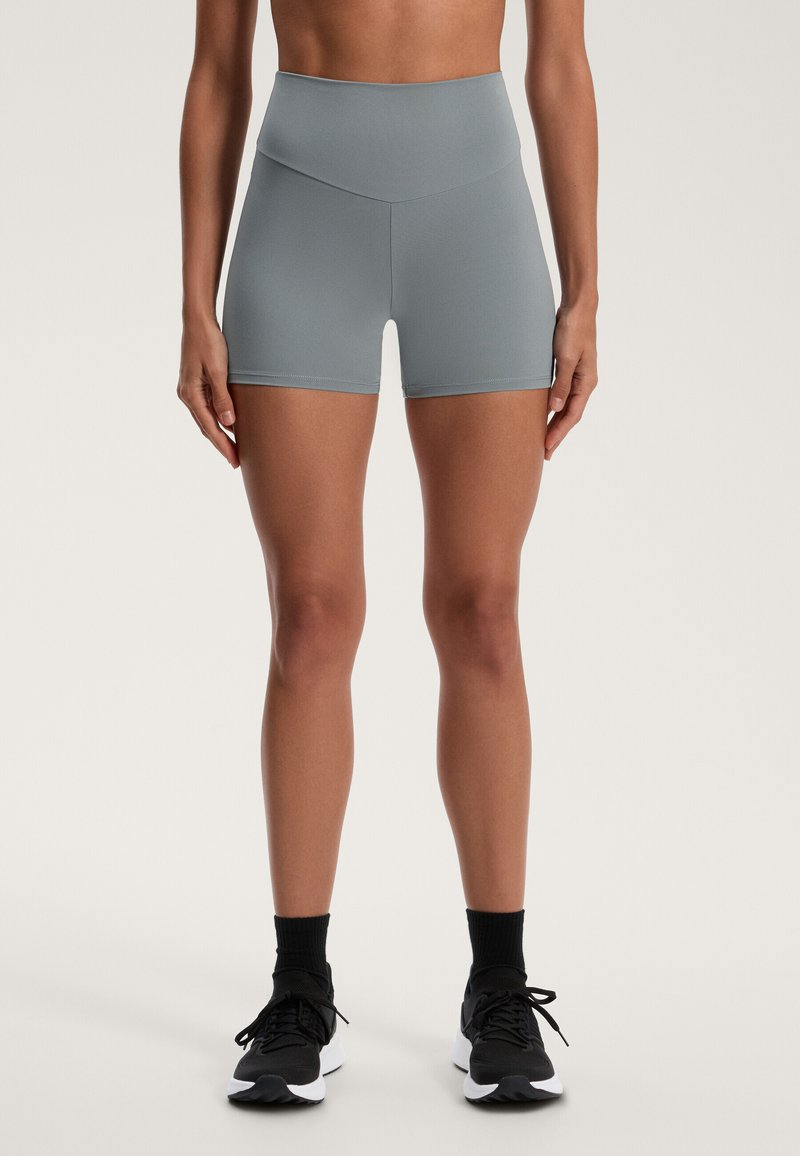Vysoké šedé športové šortky z hladkého, elastického materiálu. Majú bezšvový pás a priliehavý dizajn, doplnené čiernymi teniskami.