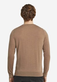 Ljusbrun tröja med långa ärmar, rund hals och en slät textur. Har ribbade muddar och nederkant, med en enkel, minimalistisk design.