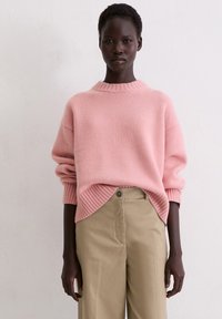 Rosa gestrickter Pullover mit einem gerippten Rundhalsausschnitt und Bündchen, kombiniert mit hoch taillierten beigen Hosen mit Knopfverschluss und geradem Bein.