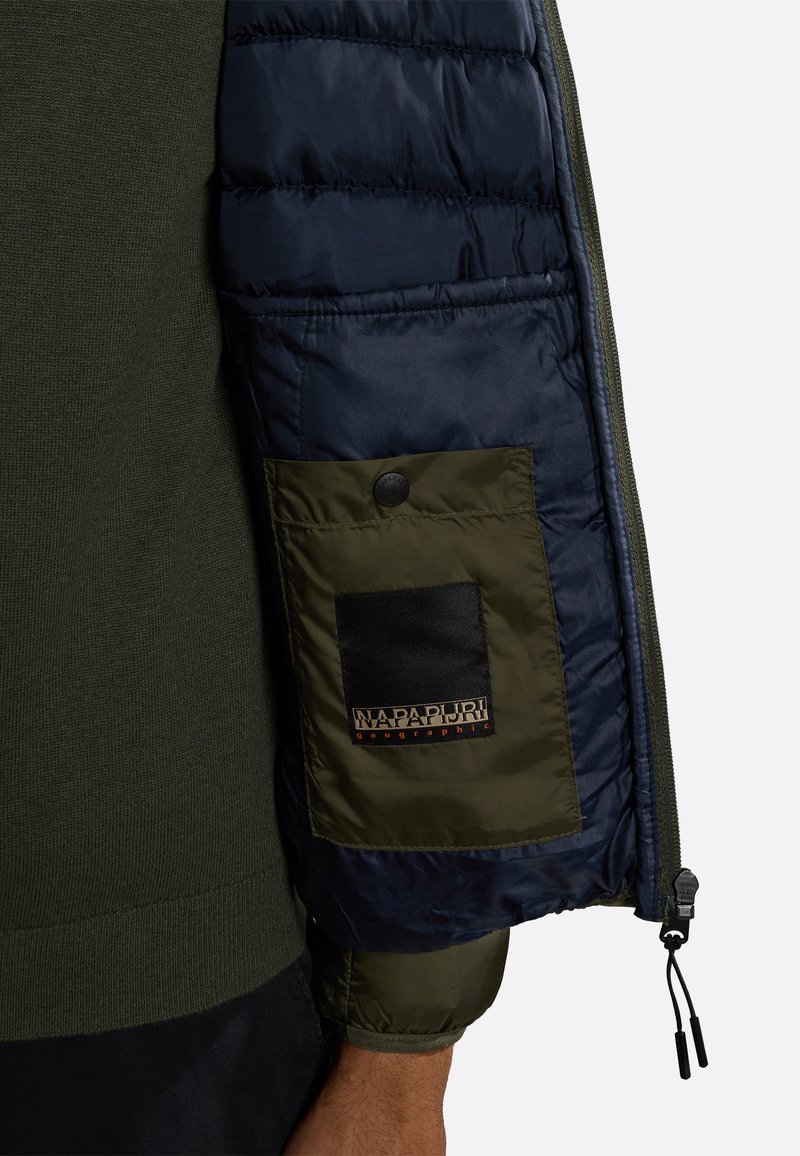 Sukienka ocieplana z ciemnoniebieskim nylonowym materiałem i oliwkowymi dzianinowymi mankietami. Posiada zapinaną na guziki kieszeń naszywaną z logo na rękawie.