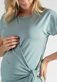 Hellblaues T-Shirt aus weichem Stoff, mit einem gedrehten Knoten-Detail an der Seite, kurzen Ärmeln und rundem Ausschnitt.