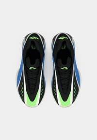 Zapatillas deportivas negras y azules con acentos verdes, parte superior de malla y superficie texturizada. Presentan un diseño aerodinámico y una suela distintiva.
