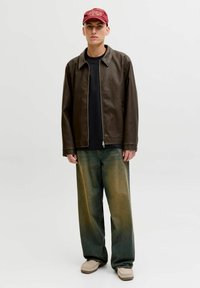 Rjava usnjena jakna na zadrgo, črna majica, izprane široke hlače z zvonci in bordo kapa z logotipom, dopolnjeni z bež obutvijo.