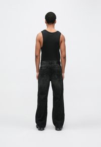 Melnā bez piedurknēm topa krekls kopā ar vaļīgām melnām džinsa biksēm, kurām ir unikāla tekstūra un šuvju detaļas aizmugurē.