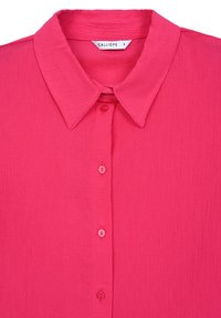 Chemise rose à col avec un tissage texturé, six boutons assortis sur le devant, et l'étiquette de la marque "CALLIOPE" à l'intérieur du col.
