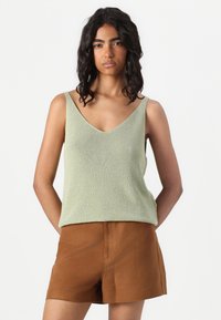 Lys grønn, ribbestrikket tanktop med V-hals og brede stropper, kombinert med brune shorts. Materialet ser glatt ut med en subtil glans.