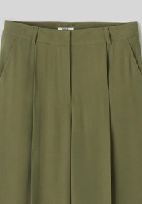 Pantalons vert olive en tissu lisse, avec un devant plat, un pli unique et des poches horizontales. Détails de couture simples.