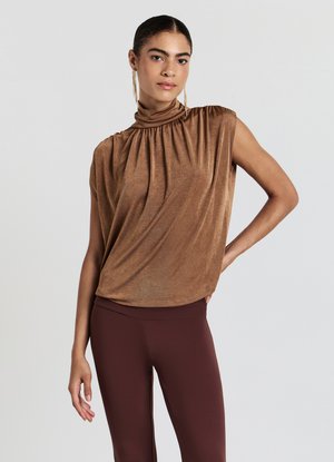 Haut sans manches en bronze avec un col montant et des détails froncés, associé à des leggings bordeaux. Tissu lisse et léger avec un subtil éclat.