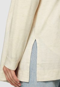 Lichtbeige lange mouw shirt van zacht materiaal, met een zijsplit en een relaxte pasvorm, gecombineerd met lichtblauwe denim.