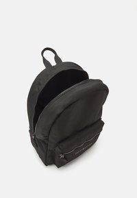 Svart tygryggsäck med rundad form, zip-prydd huvudfack och framficka. Utrustad med justerbara remmar och ett varumärkesspecifikt detaljer.